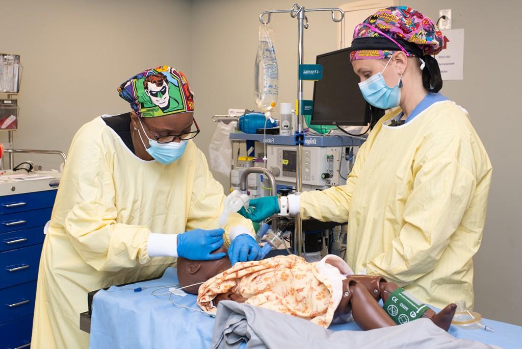 Two U N E students wearing surgical scrubs work on a patient simulator