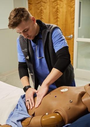 A P A student presses on a patient simulator's stomach during a lab