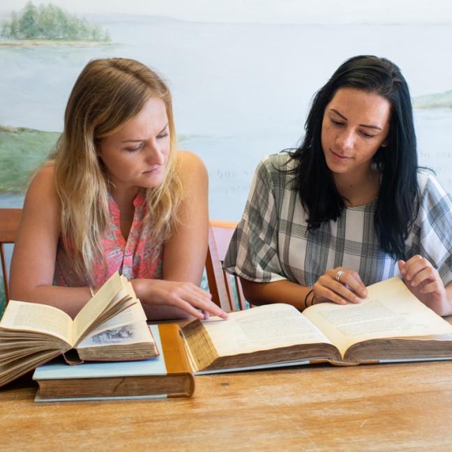 two students study together at a table with multiple books