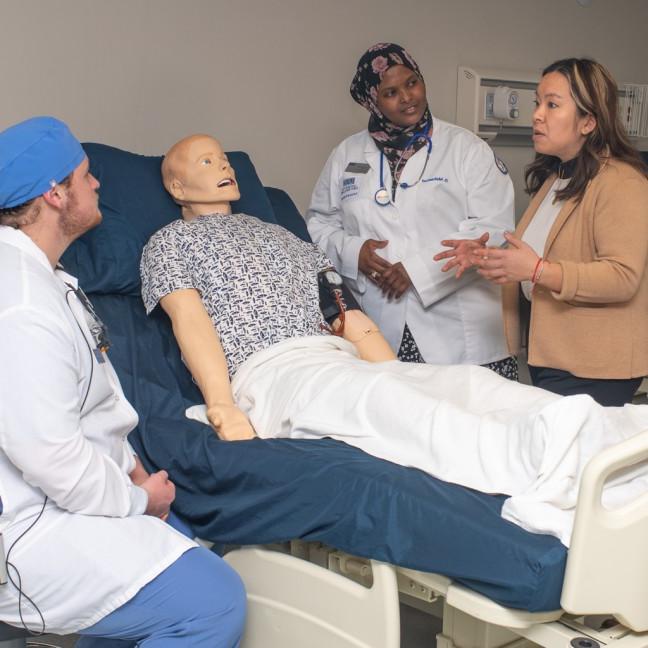 A group of students from different health programs discuss a diagnosis over a patient simulator