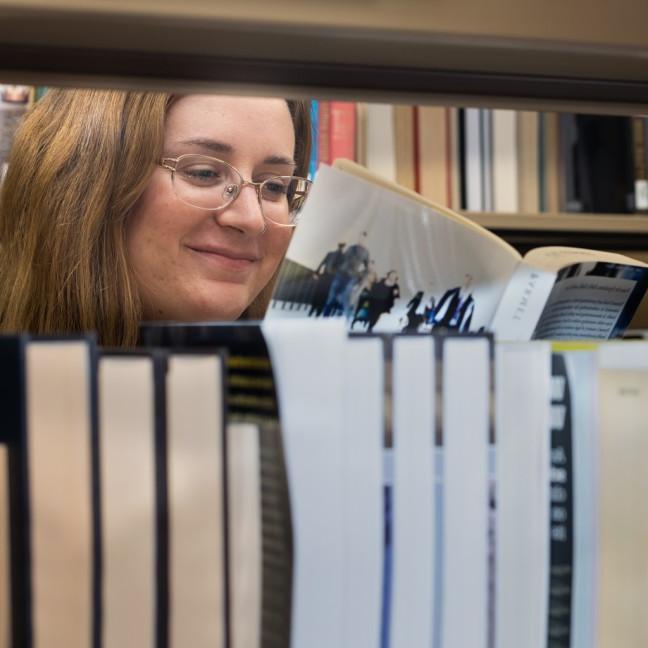 A student reading a book in the Ketchum Library library stacks